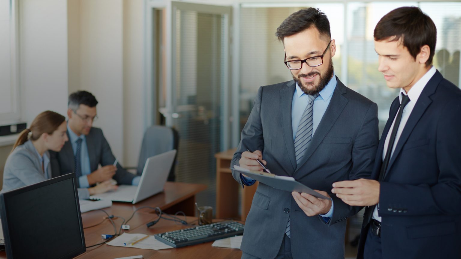 Two men in business attire standing by a computer, reviewing sustainability reports and related information.
