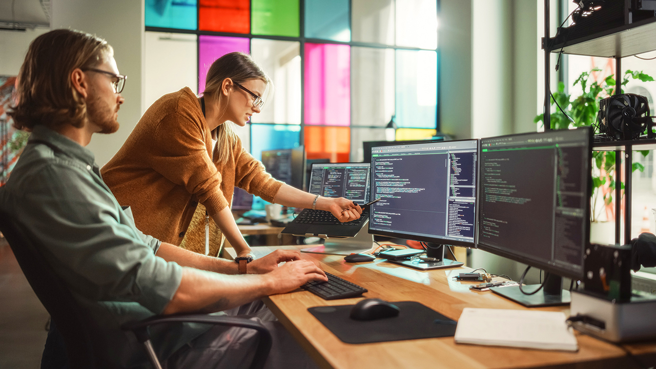 A man and a woman review data on multiple monitors, tracking efficiency and cost savings with intelligent process automation.