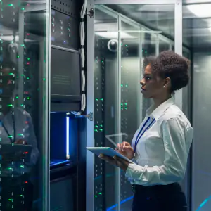 A woman in a white shirt and blue tie stands confidently in front of a server rack, symbolizing information security expertise.
