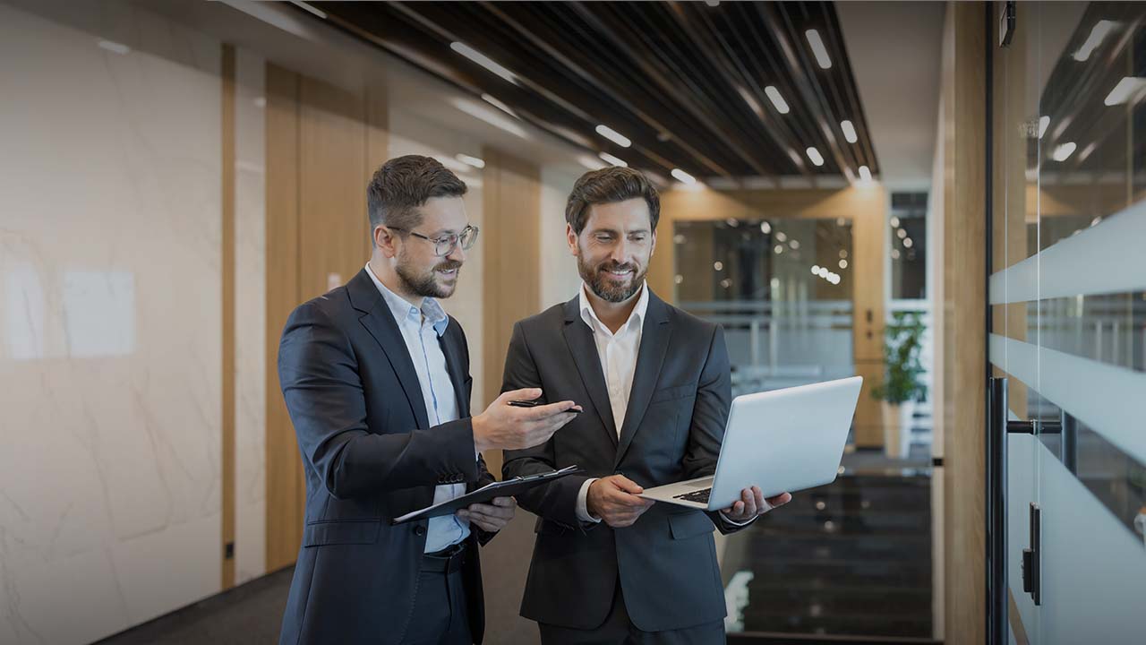 Two wealth management professionals reviewing insights on a laptop in a modern office environment.