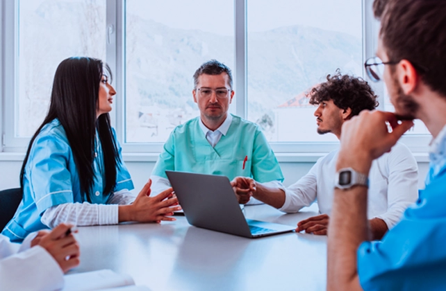 Healthcare professionals meeting around a conference table, collaborating on patient care and discussing information displayed on a laptop.