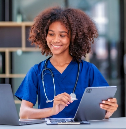 Healthcare professional using a tablet and laptop to review patient information in a clinical setting.