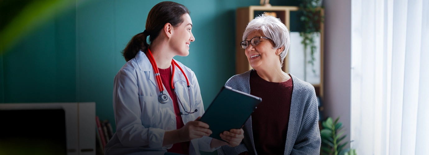 Doctor consulting with an older patient while reviewing medical information on a digital tablet in a healthcare setting.