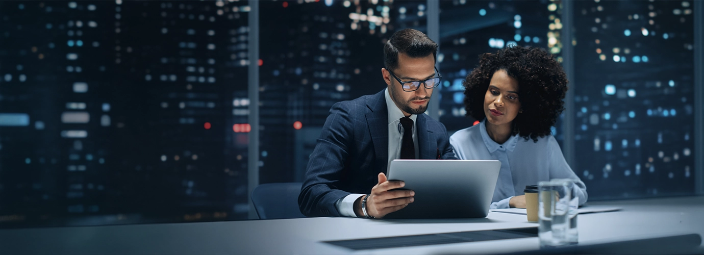 A professionally dressed man and woman seated and looking at the laptop.