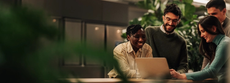 A diverse group of colleagues collaborating around a laptop in a modern office.